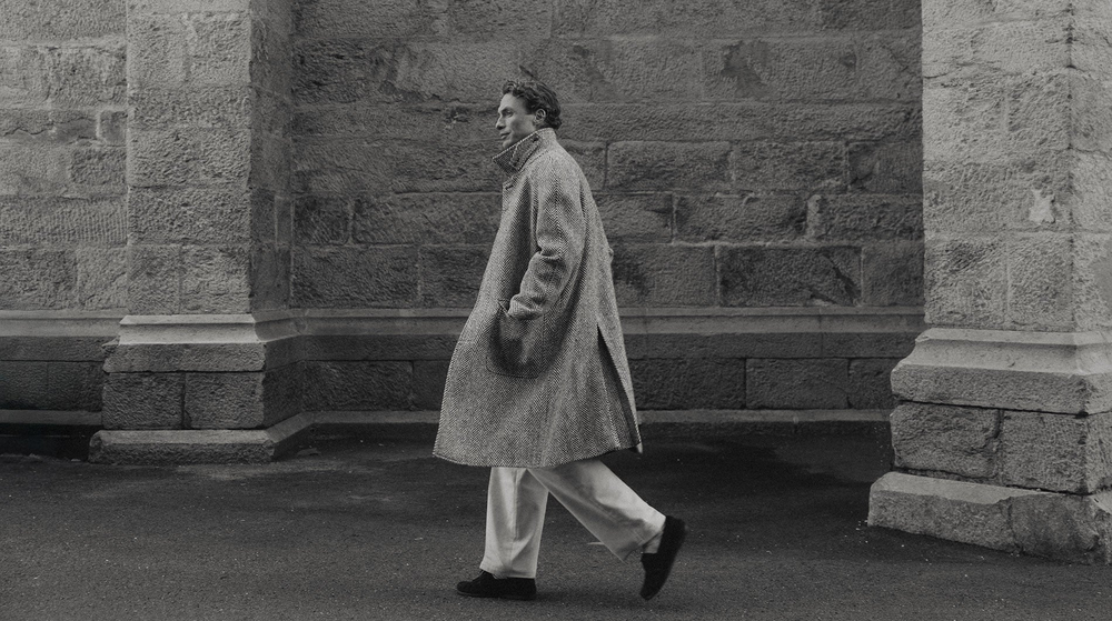 A black and white photograph of a man wearing a Berg & Berg coat and jeans.